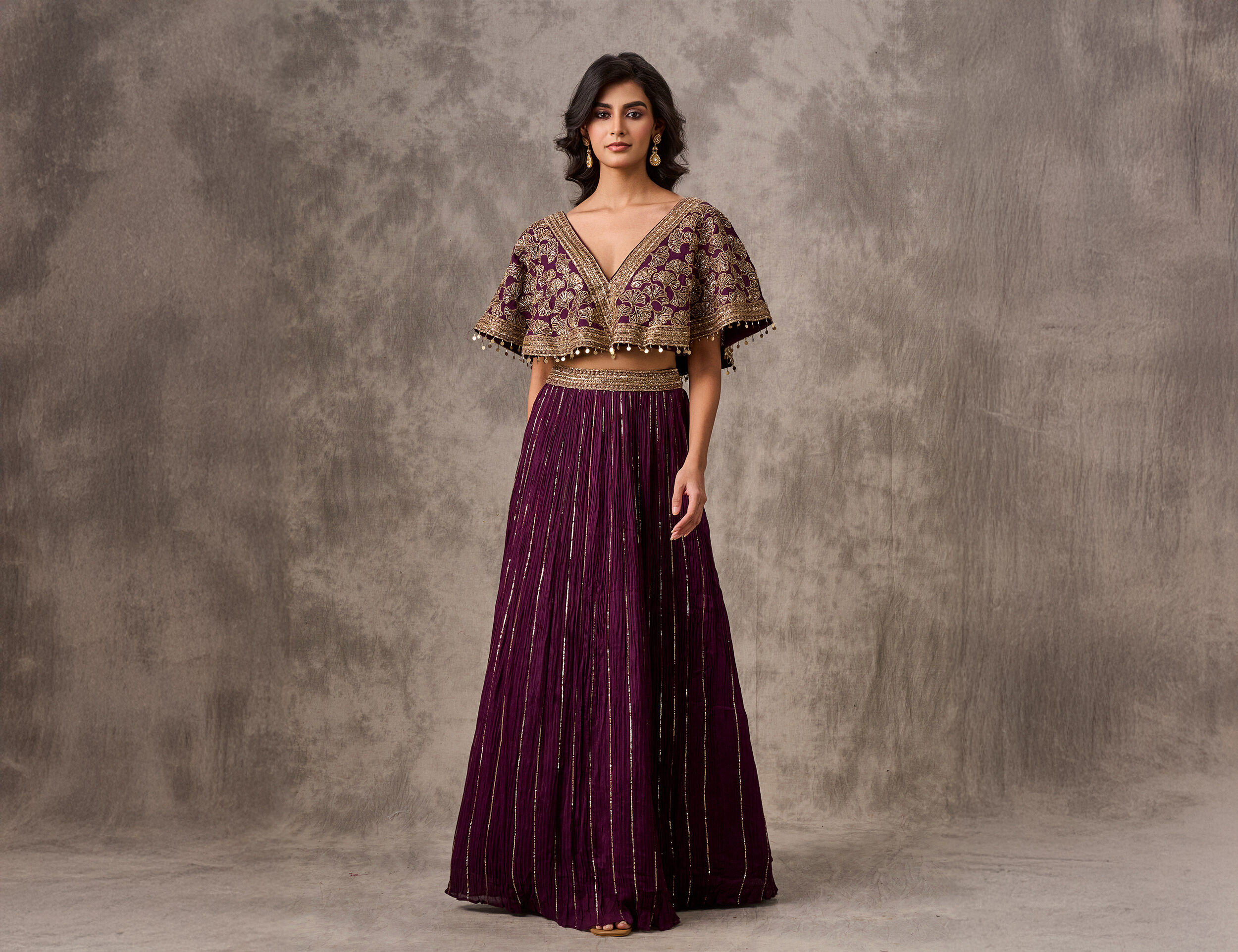 Woman in a flowing purple pleated skirt and a heavy gold embroidered cape-style blouse.